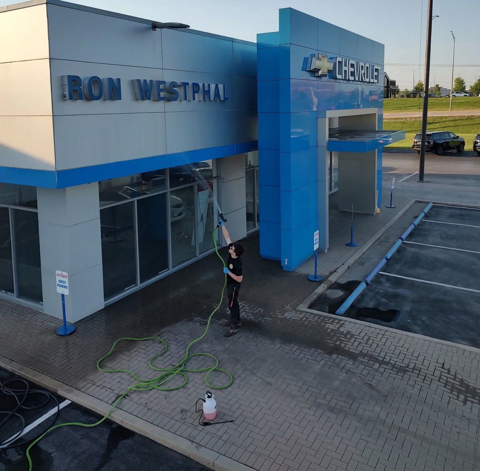 A crew member soft washing the facade of the Ron Westphal Chevrolet dealership from the ground