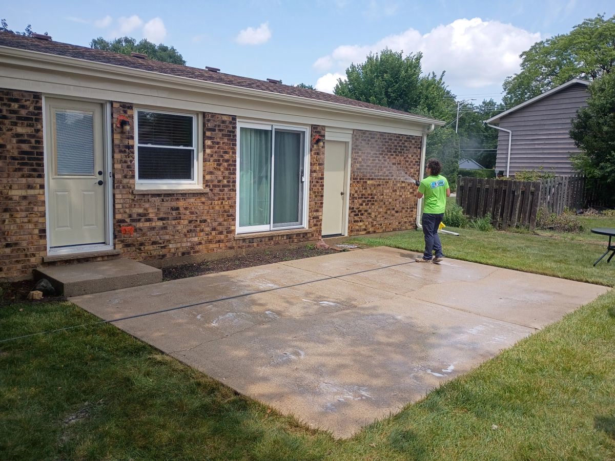 A ChicagoLand SoftWash crew member pressure washing a concrete patio behind a brick ranch home