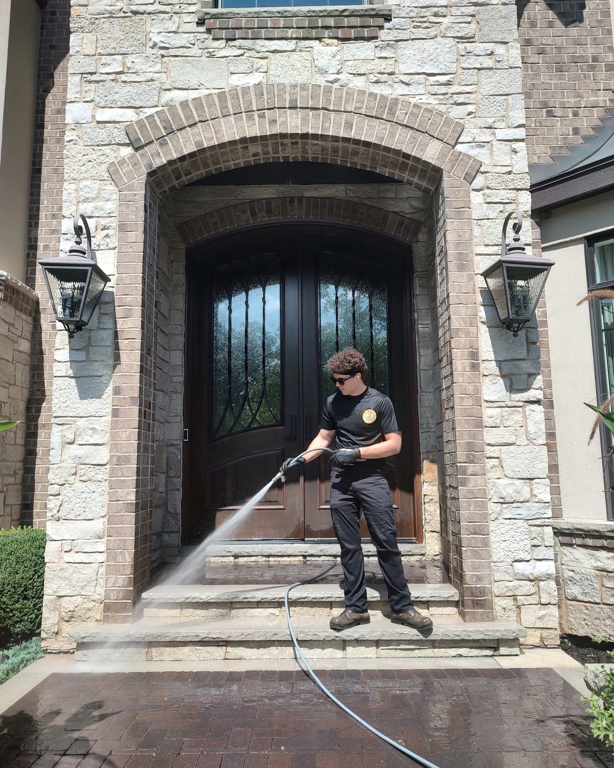 A ChicagoLand SoftWash crew member soft washing the stone-and-brick entryway of a large home