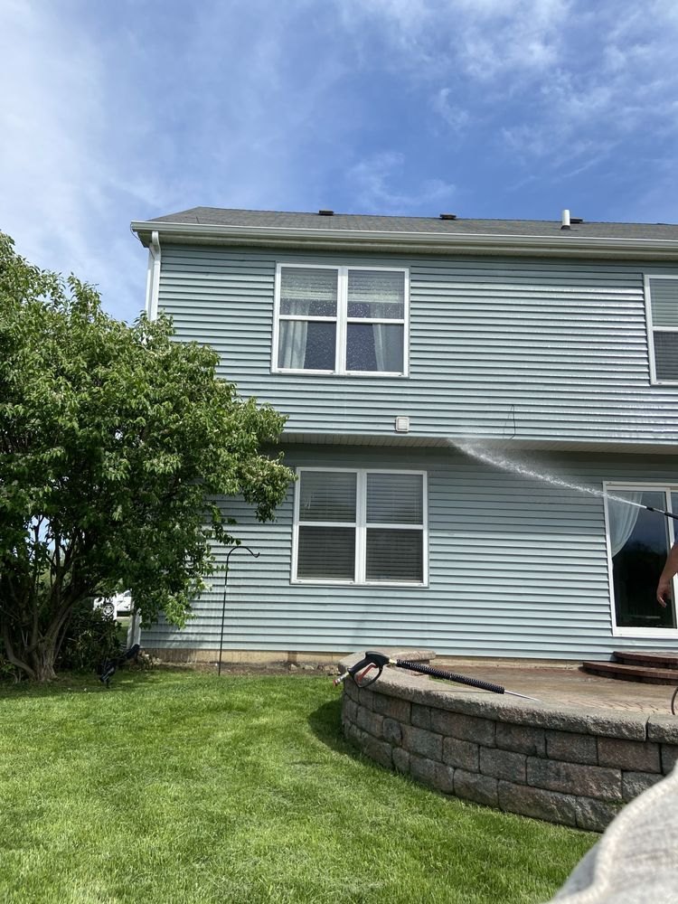 A ChicagoLand SoftWash crew member soft washing the siding of a two-story home