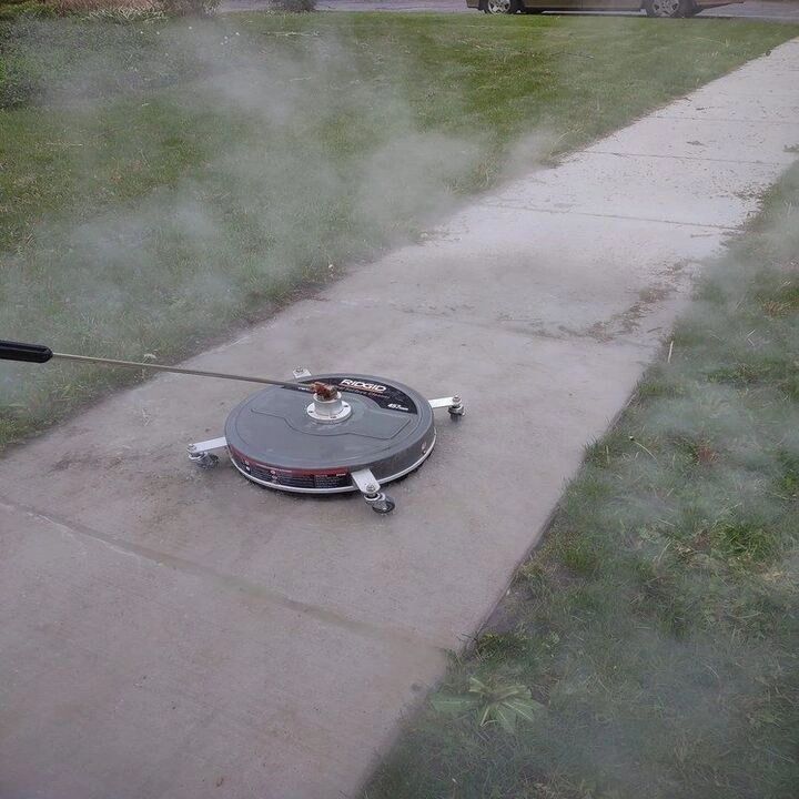 A surface cleaner mid-pass on a front walk, steam rising off the wet concrete